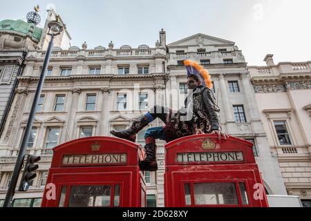 Punk-Rocker mit mohican-Haaren sitzt entspannt auf roten Telefonzellen im Zentrum von London, England, Großbritannien Stockfoto