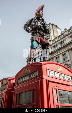 Punk-Rocker mit mohican-Haaren sitzt entspannt auf roten Telefonzellen im Zentrum von London, England, Großbritannien Stockfoto