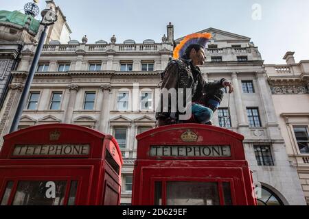 Punk-Rocker mit mohican-Haaren sitzt entspannt auf roten Telefonzellen im Zentrum von London, England, Großbritannien Stockfoto