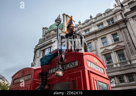 Punk-Rocker mit mohican-Haaren sitzt entspannt auf roten Telefonzellen im Zentrum von London, England, Großbritannien Stockfoto