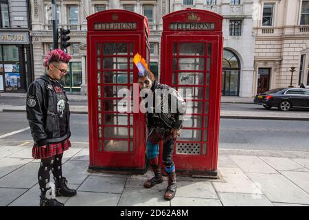 Punk-Rocker mit mohican-Haaren sitzt entspannt auf roten Telefonzellen im Zentrum von London, England, Großbritannien Stockfoto