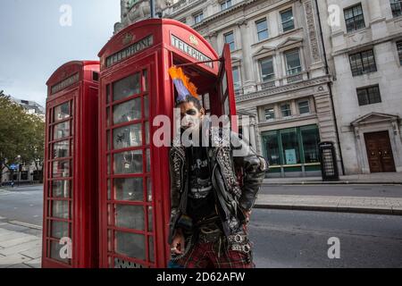 Punk-Rocker mit mohican-Haaren sitzt entspannt auf roten Telefonzellen im Zentrum von London, England, Großbritannien Stockfoto