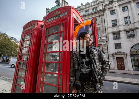Punk-Rocker mit mohican-Haaren sitzt entspannt auf roten Telefonzellen im Zentrum von London, England, Großbritannien Stockfoto