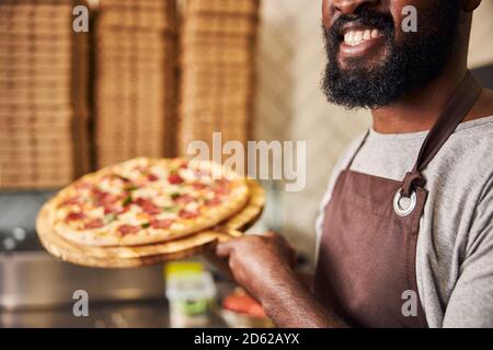 Lächelnder afroamerikanischer Mann hält Pepperoni Pizza Stockfoto