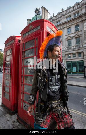 Punk-Rocker mit mohican-Haaren sitzt entspannt auf roten Telefonzellen im Zentrum von London, England, Großbritannien Stockfoto