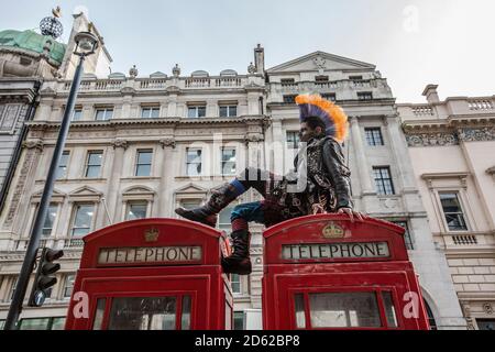 Punk-Rocker mit mohican-Haaren sitzt entspannt auf roten Telefonzellen im Zentrum von London, England, Großbritannien Stockfoto