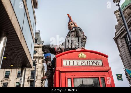 Punk-Rocker mit mohican-Haaren sitzt entspannt auf roten Telefonzellen im Zentrum von London, England, Großbritannien Stockfoto