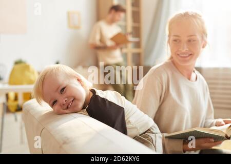 Portrait von glücklichen Baby lächelt, während seine Mutter liest ein Buch für ihn auf dem Sofa im Wohnzimmer Stockfoto