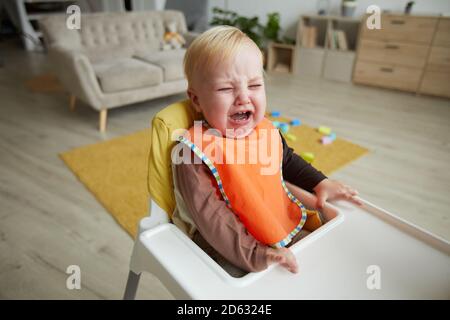 Baby Junge sitzt in Babystuhl und weint in der Zimmer Stockfoto