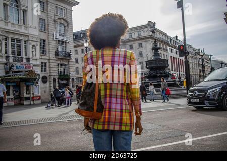Lady trägt eine bunte Jacke mit afro Frisur über die Straße zum Piccadilly Circus in London, England, Großbritannien Stockfoto