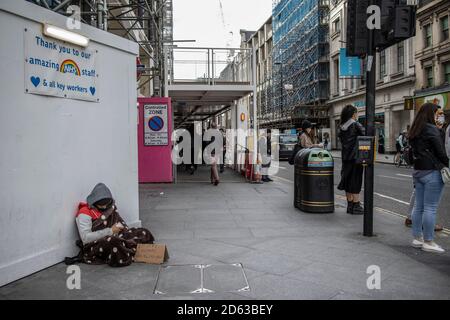 Obdachloser Mann sitzt bettelnd um Geld unter einem "Danke NHS" Schild, das an einem Arbeiter-Horten auf der Oxford Street, London, West End, England, Großbritannien angebracht ist Stockfoto