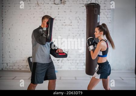 Eine junge Sportlerin in guter körperlicher Verfassung führt Kickboxen durch Training unter der Aufsicht eines erfahrenen Trainers Stockfoto