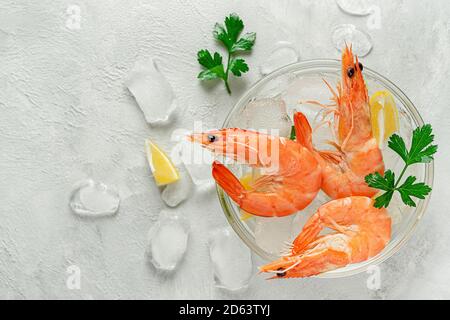 Gekühlte Garnelen in einer Schüssel mit Eis, Zitrone und Petersilie auf grauem Hintergrund. Italienisches Essen, Kopierraum. Stockfoto