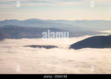 Tal bedeckt von dichtem Nebel erhellt durch goldenes Morgenlicht, Hügel erheben sich über dem Nebel und fernen Horizont Berge Stockfoto