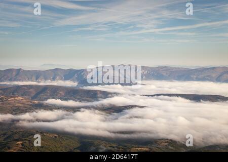 Tal bedeckt von dichtem Nebel erhellt durch goldenes Morgenlicht, Hügel erheben sich über dem Nebel und fernen Horizont Berge Stockfoto