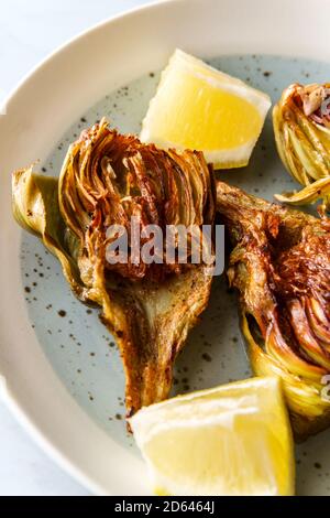 Italienische gebratene halbierte Artischocke mit Zitronenkeilen Stockfoto