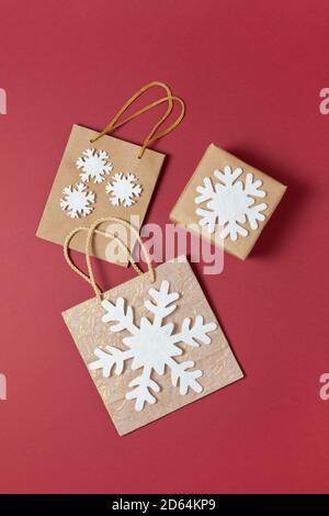 Weihnachtskomposition. Golden und Craft Urlaubspaket, hellbraune Box mit weißen Filz Schneeflocken, auf dunkelrotem Hintergrund. Konzept zur Vorbereitung von Geschenken, Stockfoto