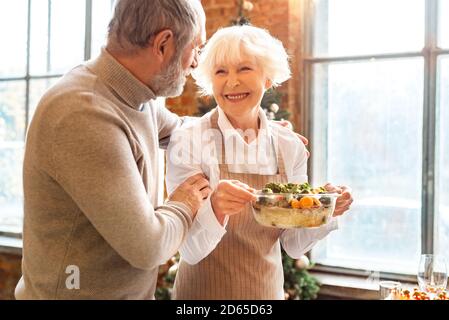 Lächelndes Seniorenpaar steht vor der Familie mit einem gesunden veganen Gericht Feiertagsdinner Stockfoto