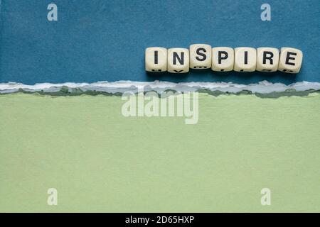 Inspire Wort abstrakt in Holzbuchstabenwürfel gegen handgemachtes Papier abstrakt in blauen und grünen Tönen, Inspiration, Führung und Rollenmodell Konzept Stockfoto
