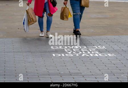 Zwei weibliche Käufer gehen an einem COVID-19 vorbei, halten Sie Abstand melden Sie sich im Stadtzentrum von Birmingham an, da strengere Beschränkungen auferlegt werden Stockfoto