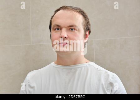 Gesicht eines Mannes in einem weißen T-Shirt, Nahaufnahme. Porträt eines 35-40-jährigen Mannes auf beigem Hintergrund Stockfoto