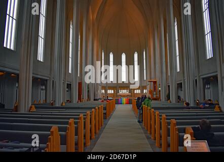 Das Innere der Hallgrimskirkja Kirche in Reykjavik. Island. Der Altar ist mit einer Regenbogenfahne (schwuler Stolz) zu sehen und Besucher versammeln sich im Inneren. Stockfoto