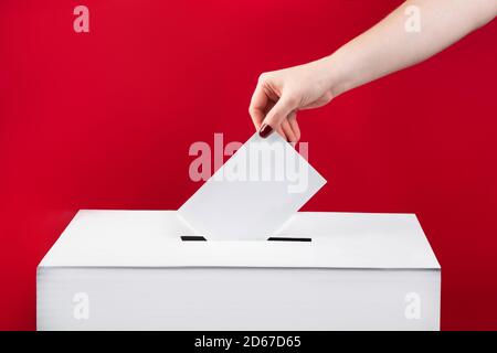 Frau legt einen Stimmzettel in die Wahlbox auf rotem Hintergrund. Wahlen in den Vereinigten Staaten. Stockfoto