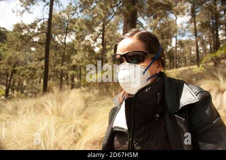 Frau mit Maske und Sonnenbrille schützt sich selbst und andere vor Coronavirus, Influenza, SARS und Atemwegserkrankungen, während sie im Wald ist Stockfoto