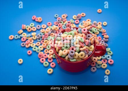 Schüssel Müsli, bunte Müsli in einer leuchtend roten Schale auf Holz, Müsli Schlaufen auf blauem Hintergrund. Schnelles Frühstück oder Snack, flat Lay. Stockfoto