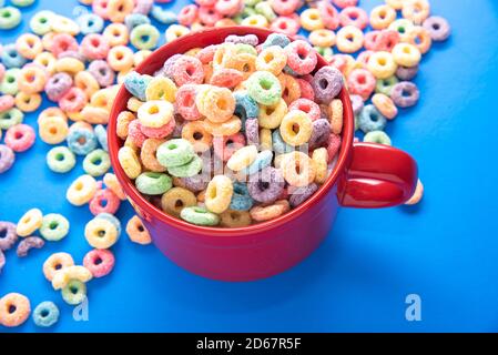 Schüssel Müsli, bunte Müsli in einer leuchtend roten Schale auf Holz, Müsli Schlaufen auf blauem Hintergrund. Schnelles Frühstück oder Snack, flat Lay. Stockfoto