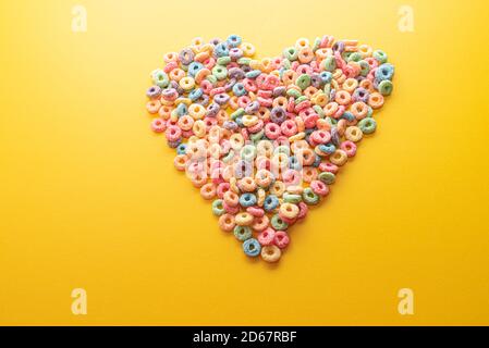 Schüssel Müsli, bunte Müsli in einer leuchtend roten Schale auf Holz, Müslischlaufen auf gelbem Hintergrund. Schnelles Frühstück oder Snack, flat Lay. Stockfoto