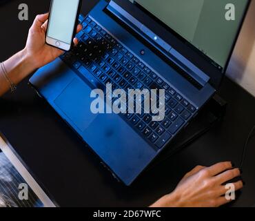 Draufsicht auf eine Frau, die mit einem Laptop arbeitet Zu Hause und etwas auf einem Smartphone zu überprüfen Stockfoto