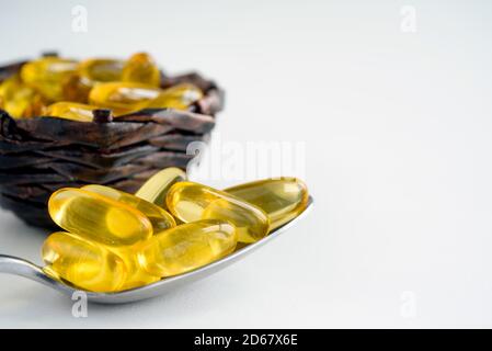 Nahaufnahme von Fischöl-Kapseln in einem Löffel und Korb auf weißem Hintergrund. Omega 3 Kapseln - natürliche Vitamine. Stockfoto