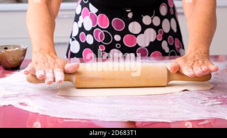 Weibliche Hände Rollen den Teig mit einem Nudelholz auf einer Holzfläche aus, Nahaufnahme. Weibliche Hände Rollen den Teig auf einem Fliedertisch. Der Koch streichelte die Hände Stockfoto