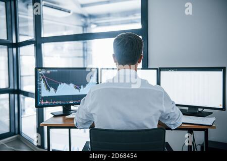Vielbeschäftigter Mitarbeiter. Blick von hinten. Der junge Geschäftsmann in formeller Kleidung ist mit mehreren Bildschirmen im Büro. Konzeption von Austausch und Geld Stockfoto