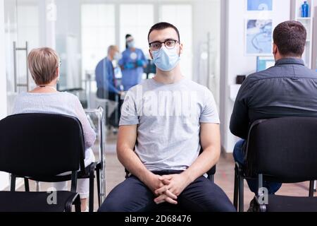 Porträt von müde jungen Mann mit Gesichtsmaske gegen Coronavirus im Krankenhaus Wartebereich Blick auf die Kamera. Senior Mann während der Konsultation im Untersuchungsraum. Stockfoto