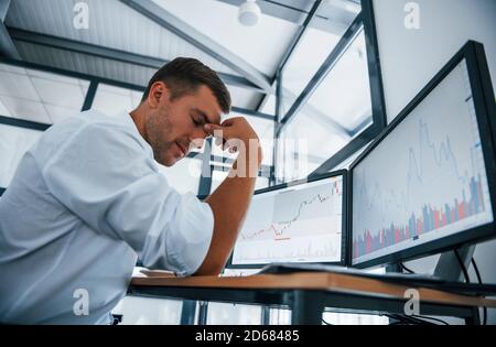 Ich fühle mich traurig. Versagen und Depression. Der junge Geschäftsmann in formeller Kleidung ist mit mehreren Bildschirmen im Büro. Konzeption von Austausch und Geld Stockfoto