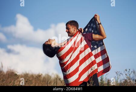 Fühlt Freiheit. Schönes Paar mit amerikanischer Flagge haben eine gute Zeit im Freien auf dem Feld Stockfoto