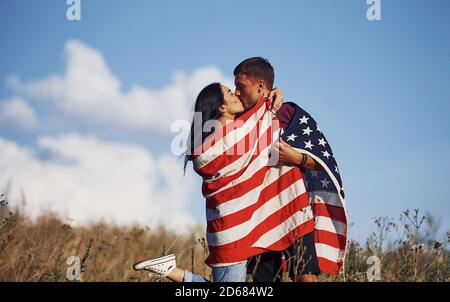 Küssen sich gegenseitig. Fühlt Freiheit. Schönes Paar mit amerikanischer Flagge haben eine gute Zeit im Freien auf dem Feld Stockfoto