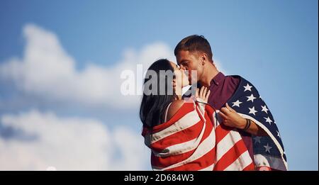 Küssen sich gegenseitig. Fühlt Freiheit. Schönes Paar mit amerikanischer Flagge haben eine gute Zeit im Freien auf dem Feld Stockfoto