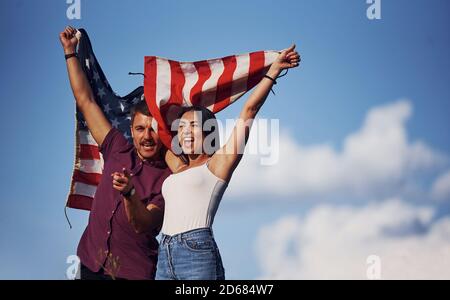 Mit den Händen nach oben. Fühlt Freiheit. Schönes Paar mit amerikanischer Flagge haben eine gute Zeit im Freien auf dem Feld Stockfoto