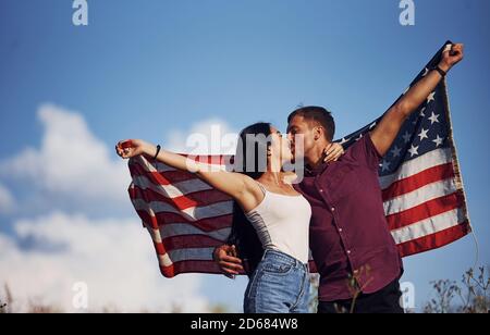 Küssen sich gegenseitig. Fühlt Freiheit. Schönes Paar mit amerikanischer Flagge haben eine gute Zeit im Freien auf dem Feld Stockfoto