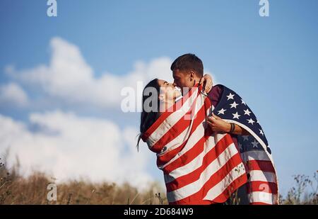 Küssen sich gegenseitig. Fühlt Freiheit. Schönes Paar mit amerikanischer Flagge haben eine gute Zeit im Freien auf dem Feld Stockfoto