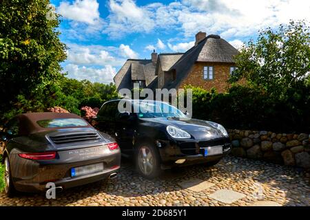 Sylt, 5. September 2020: Parken von Porsche-Autos vor einem Grundstück mit reetgedeckten Ferienhäusern auf Sylt, Deutschland Stockfoto