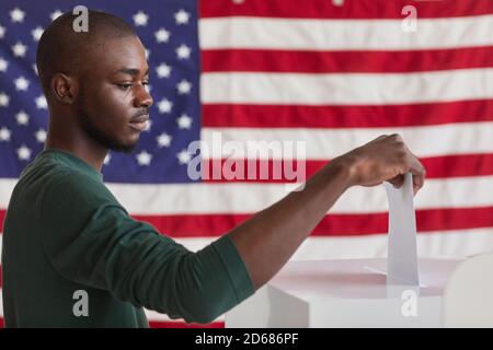 Ernster afrikanischer Mann, der den Brief in die Box während Abstimmung Stockfoto