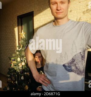 Familienpaar und Weihnachtsbaum. Ungewöhnliche Komposition, Mann im Vordergrund verschwommen, Frau im Hintergrund in mans Achselhöhle. Stockfoto