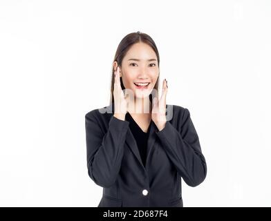 Eine hübsche junge asiatische Geschäftsfrau in schwarzem Anzug, die Hände an den Wangen mit aufgeregt lächelnd hält und die Kamera isoliert auf weißem Hintergrund anschaut. Stockfoto