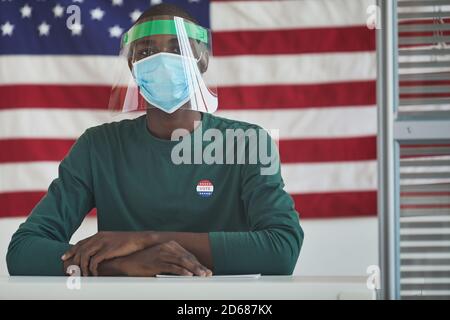 Porträt des afrikanischen Mannes in Schutzmaske sitzt an der Tabelle und Blick auf Kamera mit amerikanischer Flagge in der Hintergrund Stockfoto