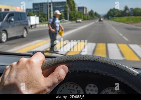 Fahrer Hand auf das Lenkrad eines Autos gegen Der Hintergrund eines Fußgängers, der durch eine Zebrakreuzung geht Stockfoto