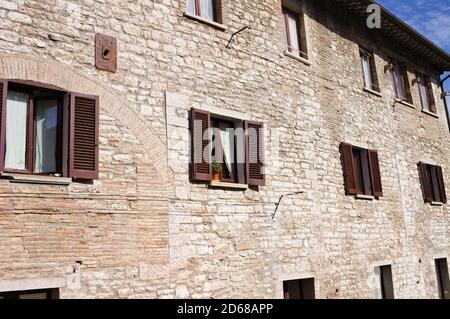 Eine Reihe von Fenstern mit braunen hölzernen Fensterläden in einer alten Ziegelmauer in einem mittelalterlichen Dorf (Gubbio, Umbrien, Italien, Europa) Stockfoto